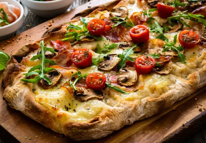 Pyszna pizza bez drożdży z pomidorkami, pieczarkami i rukolą na drewnianej desce.