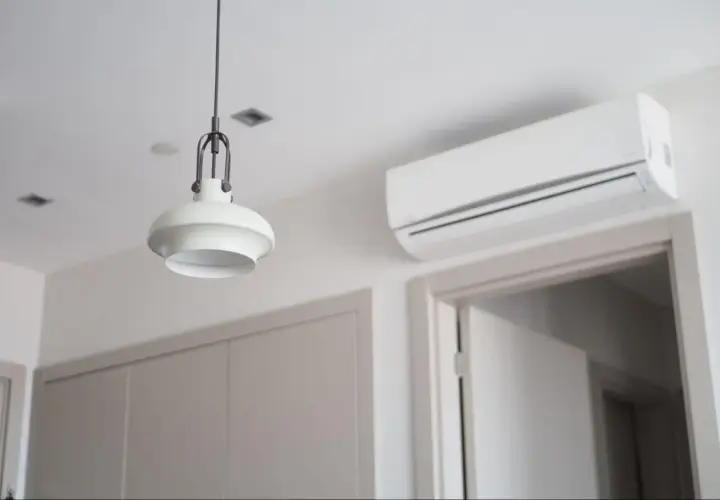 Biała klimatyzacja ścienna nad drzwiami, obok lampy wiszącej.