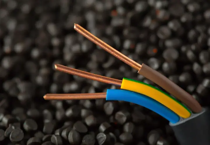 Trzy miedziane żyły kabla elektrycznego, izolowane brązowym, żółto-zielonym i niebieskim przewodem, na tle granulatów tworzywa sztucznego. Idealne do instalacji IP20.