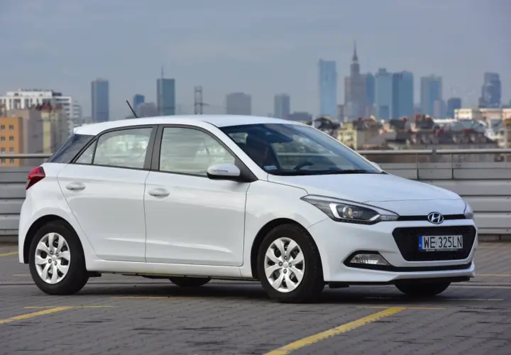 Biały Hyundai i20 zaparkowany na parkingu z widokiem na miasto w tle.