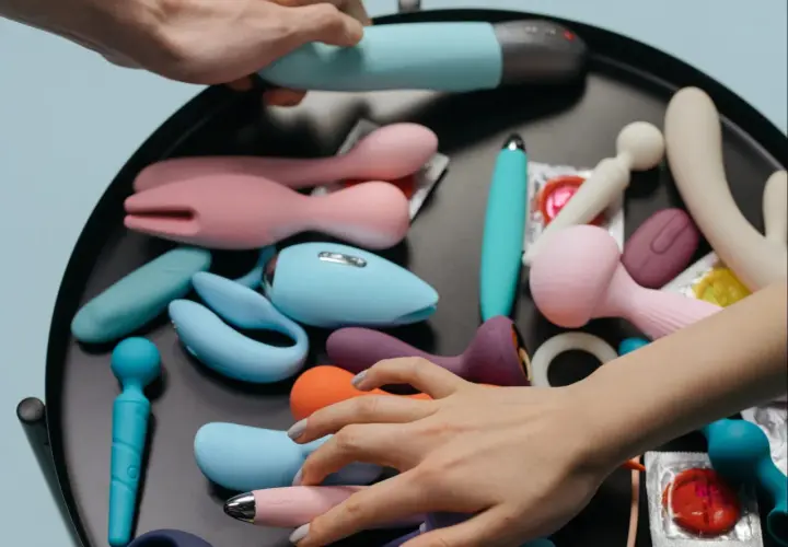 Mani che scelgono tra vari vibratori e sex toys, suggerendo la masturbazione femminile.