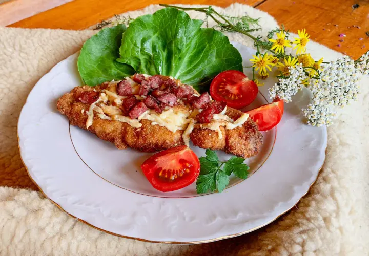 Schab po góralsku, panierowany kotlet z serem i boczkiem, podany z pomidorami i sałatą.