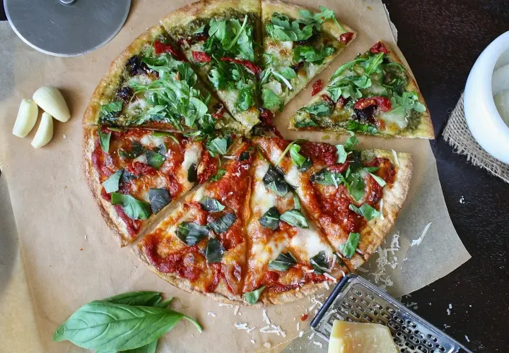 Dwie połówki pizzy: jedna z pesto i rukolą, druga z sosem pomidorowym i bazylią. Zastanawiasz się, ile kosztuje pizza w Czechach?