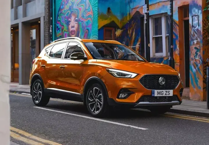 Pomarańczowy MG ZS na tle kolorowego muralu. Sprawdź nasze samochody MG opinie i przekonaj się sam!