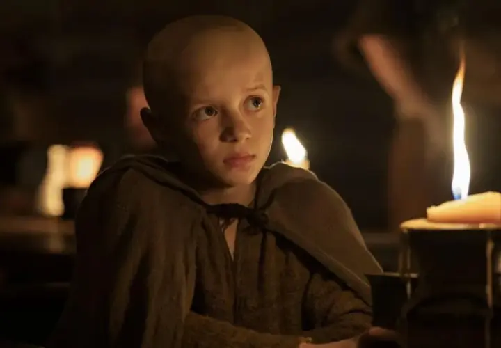 Un jeune garçon chauve, vêtu d'une tunique marron, regarde fixement une bougie allumée. Scène de "A Knight of the Seven Kingdoms Episode 3".
