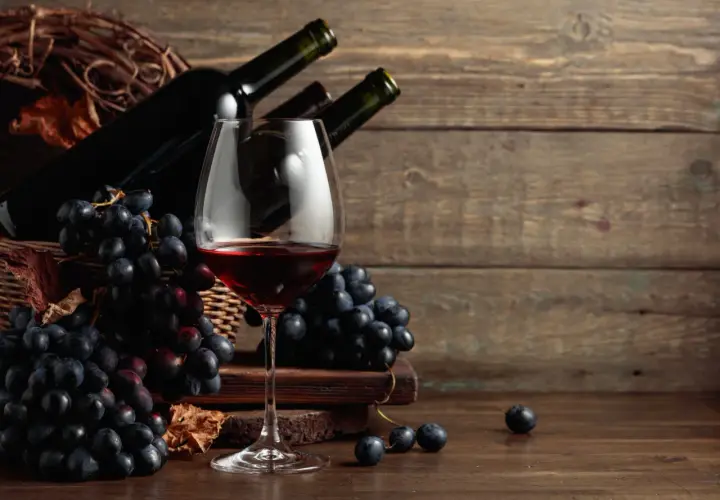 Calice di vino rosso, grappoli d'uva nera e bottiglie in un cesto. Ideale per scoprire i migliori sassicaia abbinamenti.