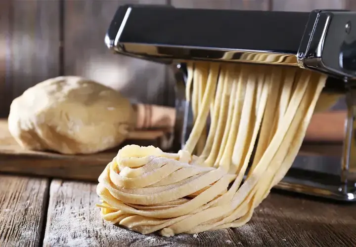 Świeży, swojski makaron powstaje w maszynce. Obok ciasto i gotowe tagliatelle. Idealny przepis na domowy makaron.
