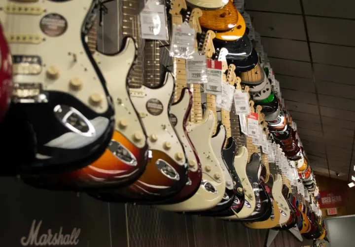 Rząd gitar elektrycznych w sklepie, idealnych jako jaka gitara elektryczna na początek. Różne kolory i modele wiszą na ścianie.