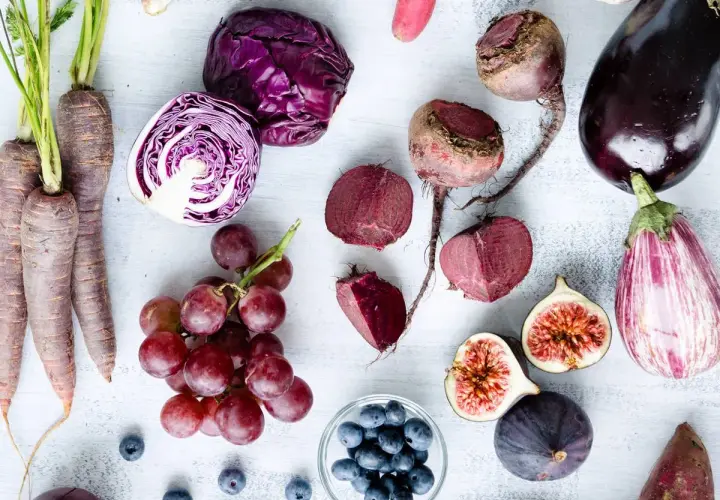 Un surtido de verduras raras y frutas moradas: zanahorias, col lombarda, remolachas, berenjenas, higos, uvas y arándanos.