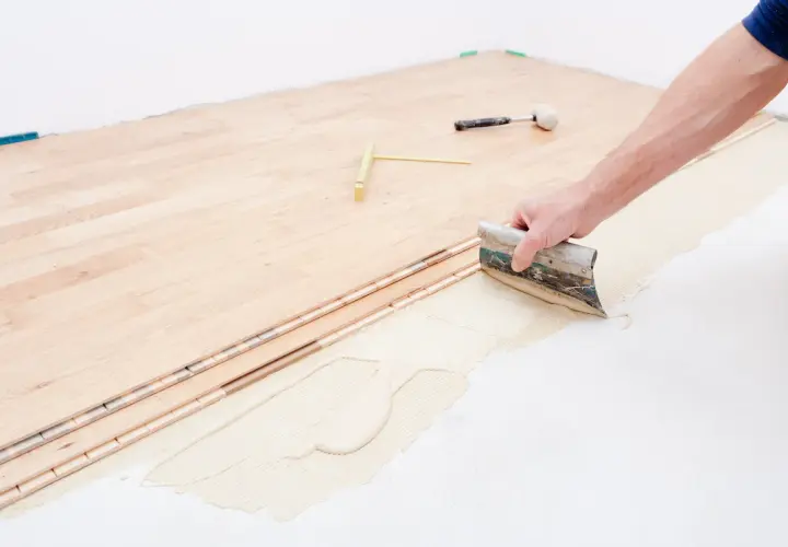 Pose d'un plancher bois étage : application de colle avec une spatule sur le support avant la pose des lames.