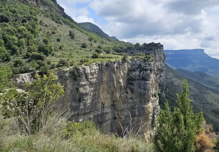 Impresionante pared rocosa del salt de sallent, con vegetación verde y un cielo nublado.