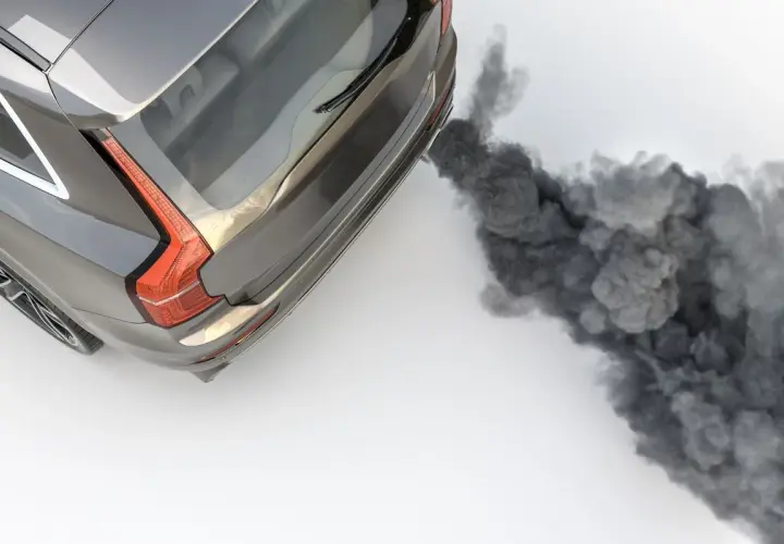 Un coche emite una densa nube de humo negro por el tubo de escape al acelerar, contaminando el aire.