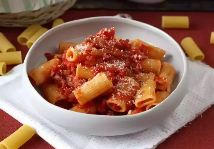 Pyszne rigatoni amatriciana, bogato polane sosem pomidorowym z guanciale i posypane parmezanem, w białej misce.