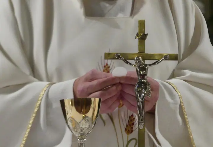 Ksiądz trzyma hostię i krzyż. Złoty kielich stoi obok. Zastanawiasz się, ile trwa msza?