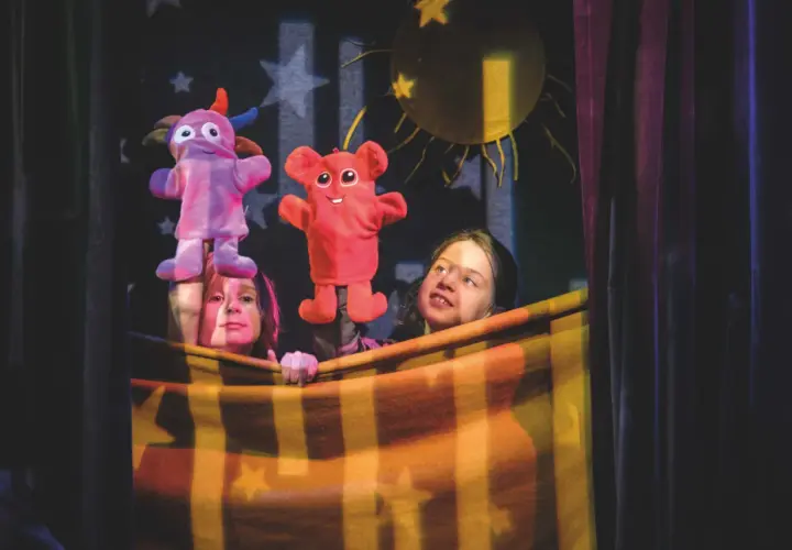 Två barn bakom en filt uppför dock teater med färgglada figurer.