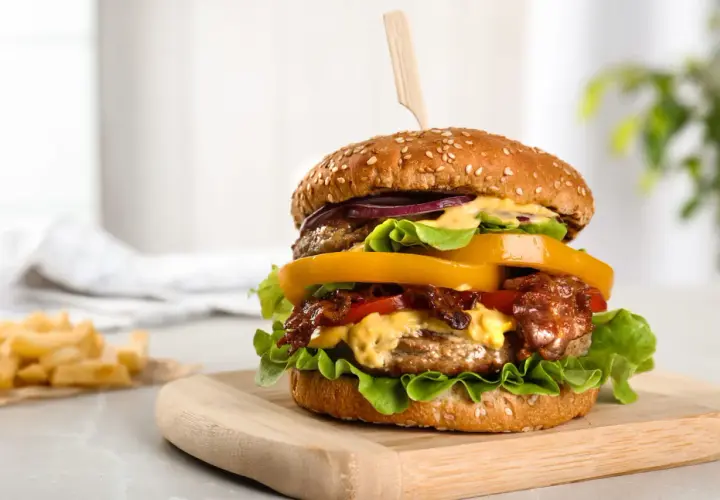 Un délicieux hamburger au barbecue, garni de bacon croustillant, de fromage fondant et de légumes frais, servi sur une planche en bois.