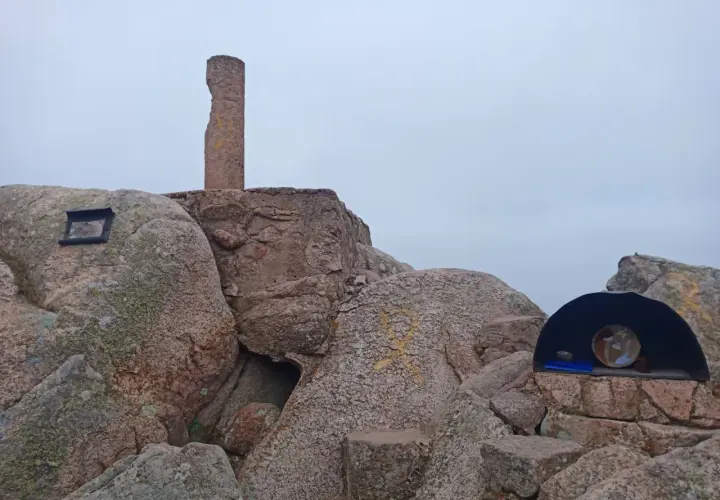 Cima del Puig de Cadiretes con un monolito, rocas y un pequeño refugio con un objeto en su interior.