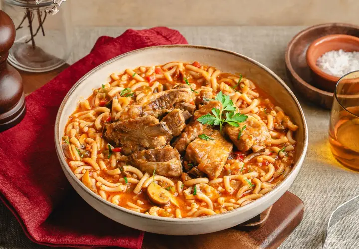 Un reconfortante plato de fideos a la cazuela con costilla, servido en un cuenco rústico, con un toque de perejil fresco.