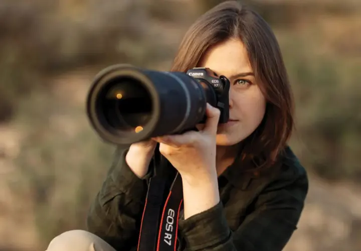 Kobieta z aparatem Canon EOS R7, gotowa do zrobienia idealnego ujęcia. To świetny materiał na poradnik fotograficzny.