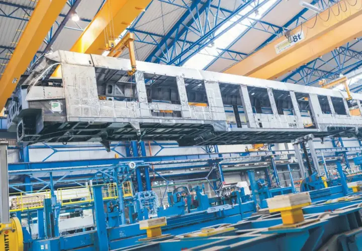 Szkielet wagonu kolejowego w hali produkcyjnej Alstom Chorzów, unoszony przez suwnicę.
