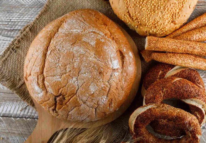Różne rodzaje pieczywa: bochenek, paluszki sezamowe, obwarzanki i chleb z ziarnami.