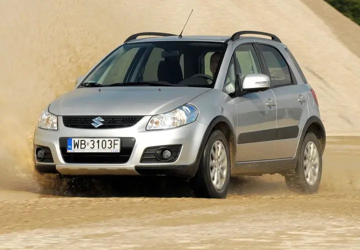 Srebrny Suzuki SX4 1.6 benzyna pokonuje piaszczystą wydmę, wzbijając tumany piasku.
