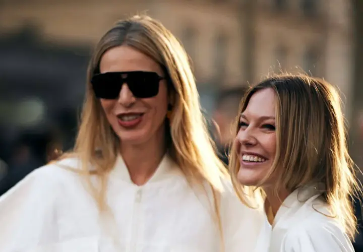 Dos mujeres sonríen, una con gafas de sol y pelo liso rubio, la otra con pelo liso castaño.