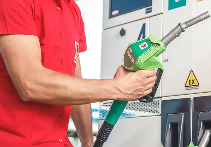 Un uomo in camicia rossa tiene una pompa di benzina verde con la scritta "Super 95".