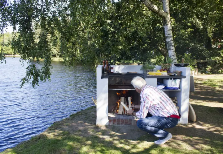 Man tänder en murad grill vid en sjö.