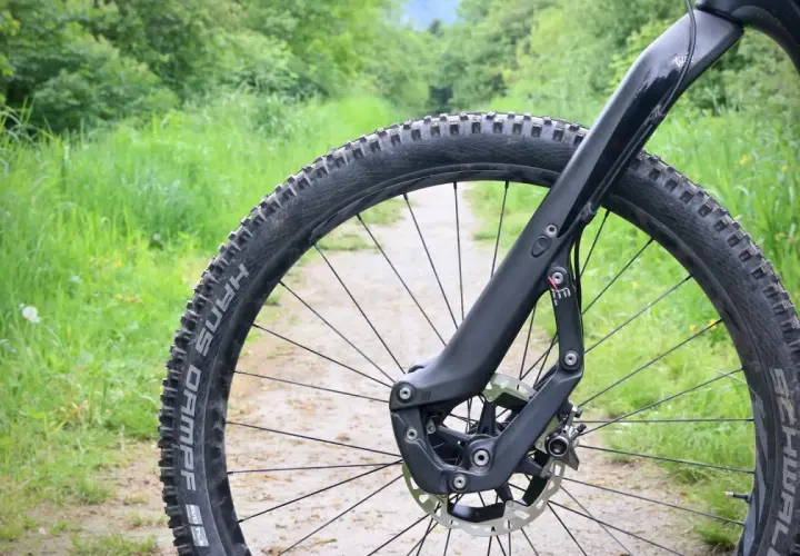 Close-up of a mountain bike's front wheel and fork on a dirt path, ready for adventure. This setup inspires trust and performance on any trail.