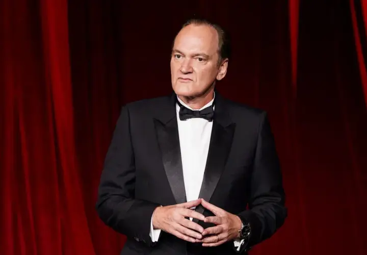 Quentin Tarantino, ikonen bakom ikoniska tarantino filmer, i en elegant smoking framför en röd ridå.