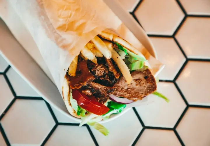 Kebab na talerzu z mięsem, frytkami, sałatą i pomidorem, zawinięty w papier.