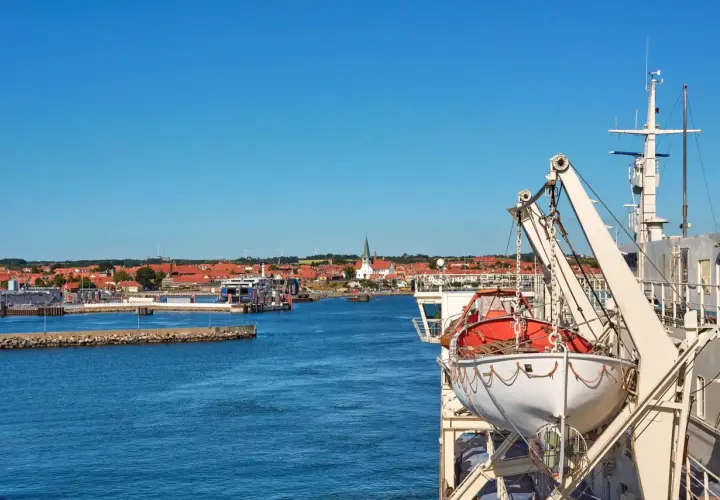 Widok na port z promem, łodzią ratunkową i miastem w tle.