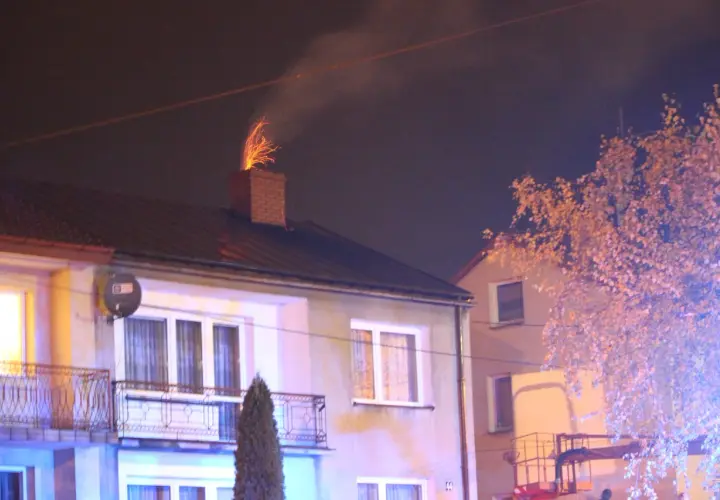 Jasny komin z cegły, z którego lecą iskry, sugeruje, dlaczego lecą iskry z komina. W tle widać dom i drzewo.