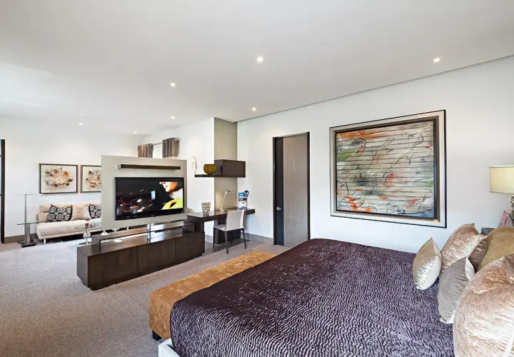 Modernes Schlafzimmer mit einem großen Fernseher im Wohnbereich, der durch eine Trennwand vom Bett abgetrennt ist.