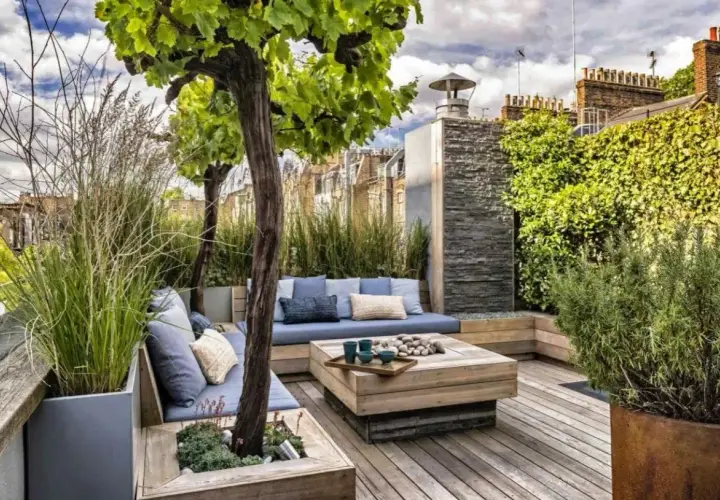 Aménagement autour d'une terrasse avec banquette bleue, table basse en bois et végétation luxuriante. Un espace détente chic et verdoyant.
