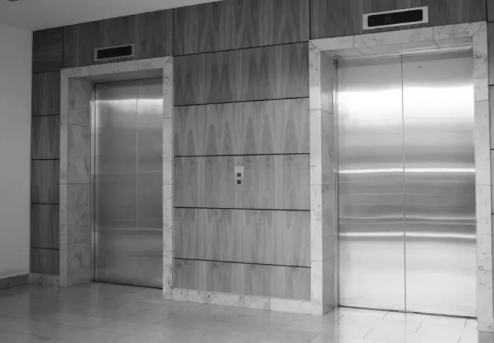 Dos ascensores modernos con puertas de acero inoxidable. Los ascensores tienen cámaras de seguridad integradas en el panel superior.