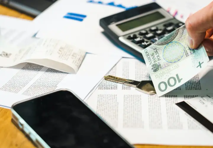 Dłoń trzyma banknot 100 zł obok klucza i dokumentów. Rozważasz grupy podatkowe darowizna?