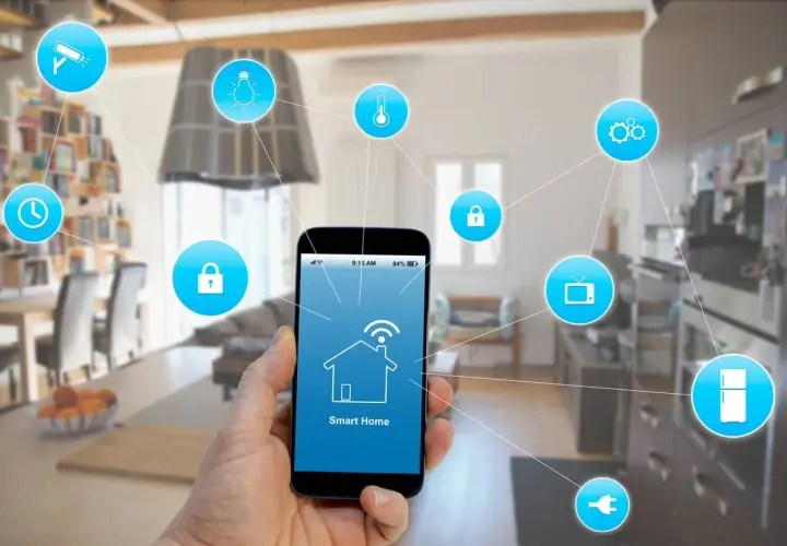 Mano sujetando smartphone con app "Smart Home" para control de instalación domótica. Iconos de seguridad, luz, temperatura, TV, nevera y enchufe conectados.