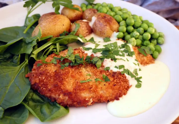 Krispig schnitzel med krämig sås till, serverad med småpotatis, gröna ärtor och färsk spenat.