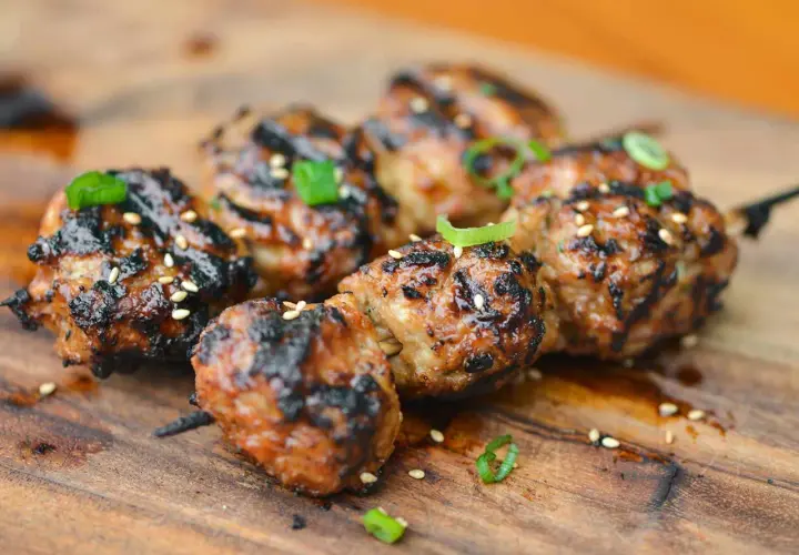 Skewered, grilled Japanese meatballs glazed with a savory sauce, sprinkled with sesame seeds and green onions.