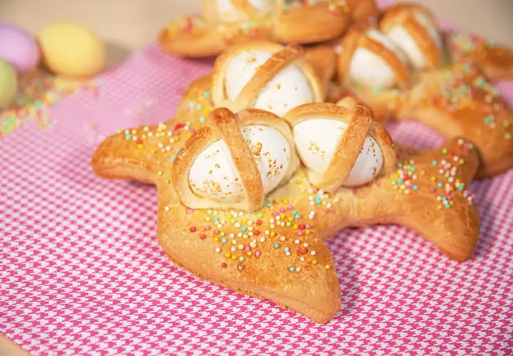 Scarcelle pugliesi ricetta originale: dolci a forma di colomba con uova sode, decorati con zuccherini colorati su tovaglia a quadretti rosa.