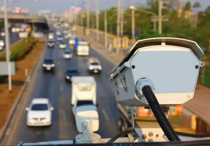 Kamera monitorująca ruch drogowy. Czy policja może wykryć antyradar? Zbliżenie na białą kamerę z kablem, w tle ruchliwa autostrada.