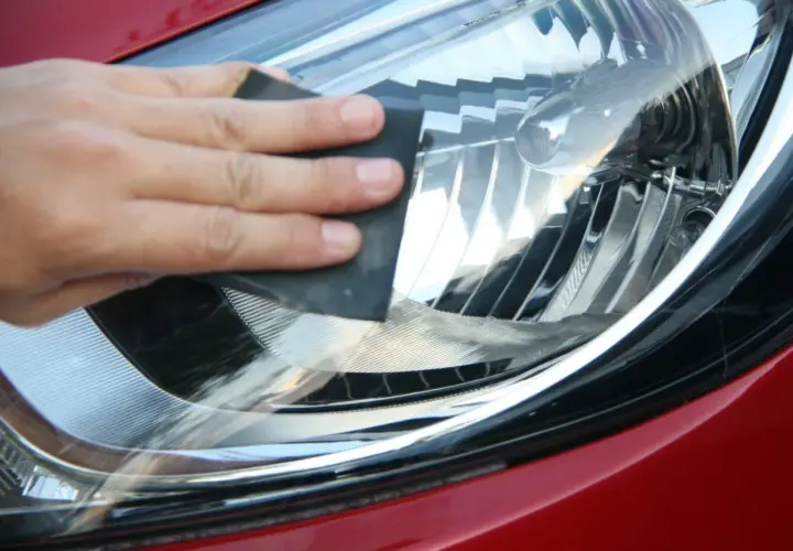 Dłoń szlifuje reflektor papierem ściernym. Po polerowaniu lampy warto zabezpieczyć je specjalnym lakierem lub folią ochronną.