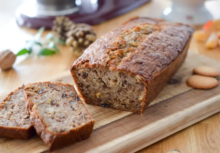 Un délicieux cake banane, coupé en tranches, sur une planche en bois. Des noix et des biscuits complètent cette gourmandise.