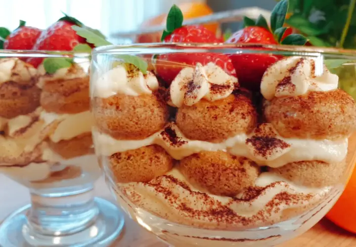 Pyszne tiramisu w pucharkach, przełożone kremem i biszkoptami, ozdobione truskawkami i kakao.