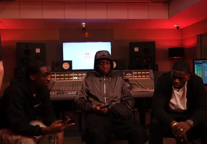 Trois jeunes hommes dans un studio d'enregistrement, discutant peut-être d'un cover rap gratuit.