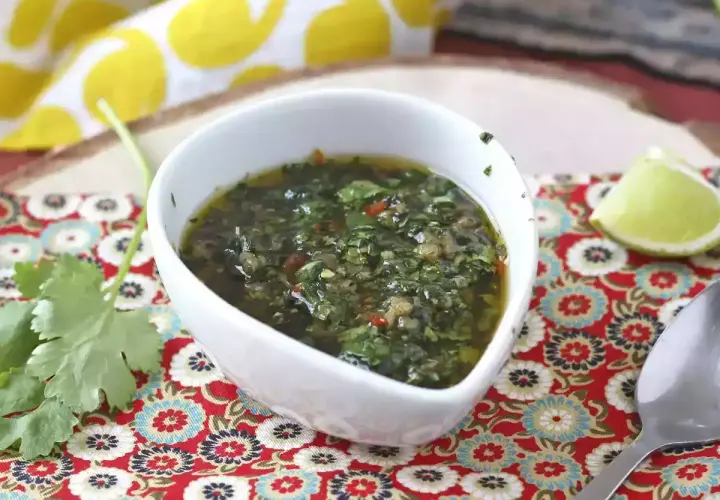 Un tazón blanco con una deliciosa **receta de chimichurri** casera, adornado con cilantro fresco y una rodaja de limón.