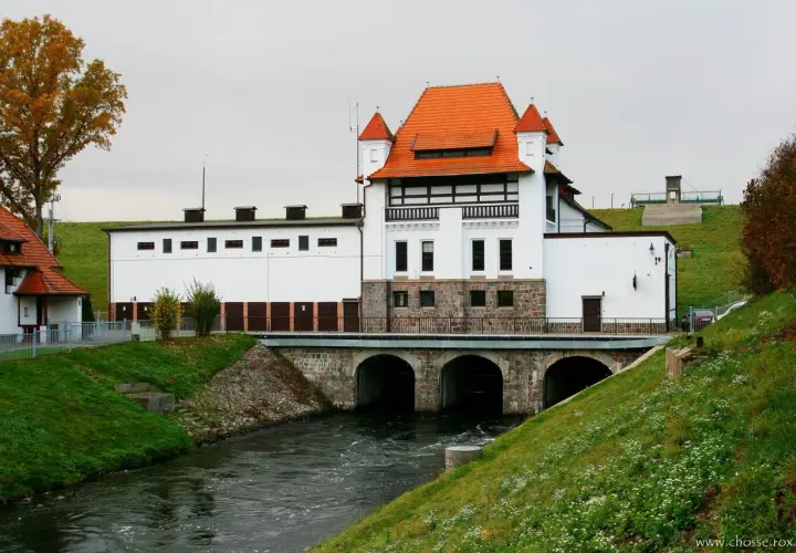 Elektrownia wodna Straszyn z charakterystycznym czerwonym dachem i kamienną podstawą, nad rwącą rzeką.