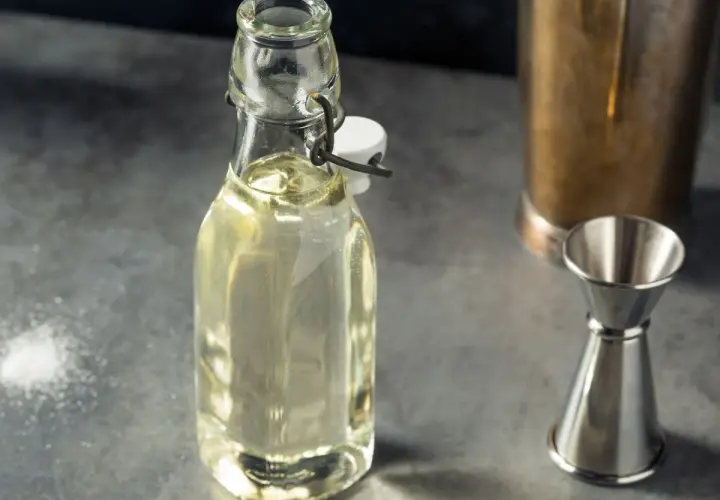 Domowy syrop cukrowy (simple syrup) w butelce, obok jigger i shakera. Idealny do drinków, łatwy do przygotowania krok po kroku.